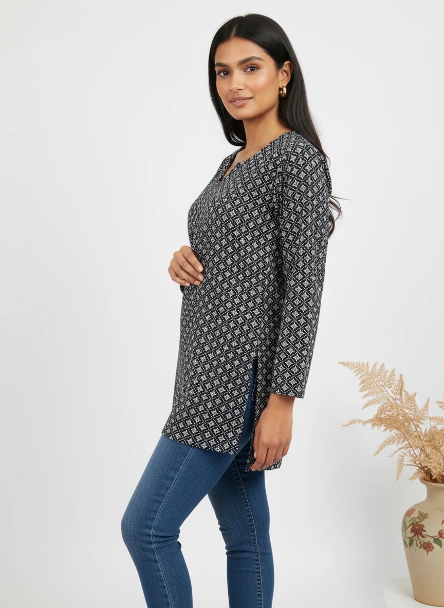 A woman wearing a black and white patterned tunic top with side slits and blue jeans against a neutral studio background.