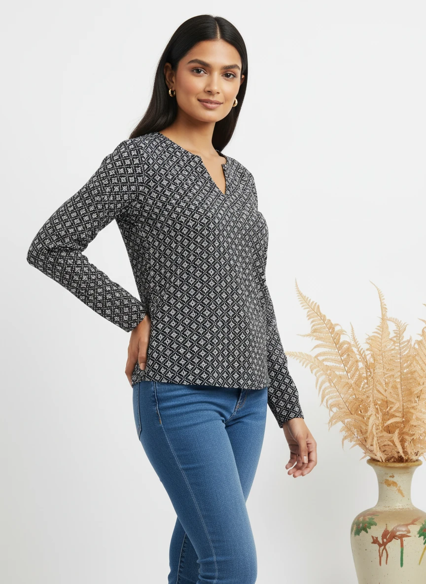 Woman wearing a black printed long-sleeve top and blue jeans, posing in a studio with a decorative vase.