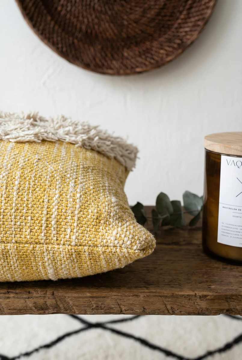 Sanskriti textured yellow and white woven cushion with fringe detail placed on a wooden bench near a candle.