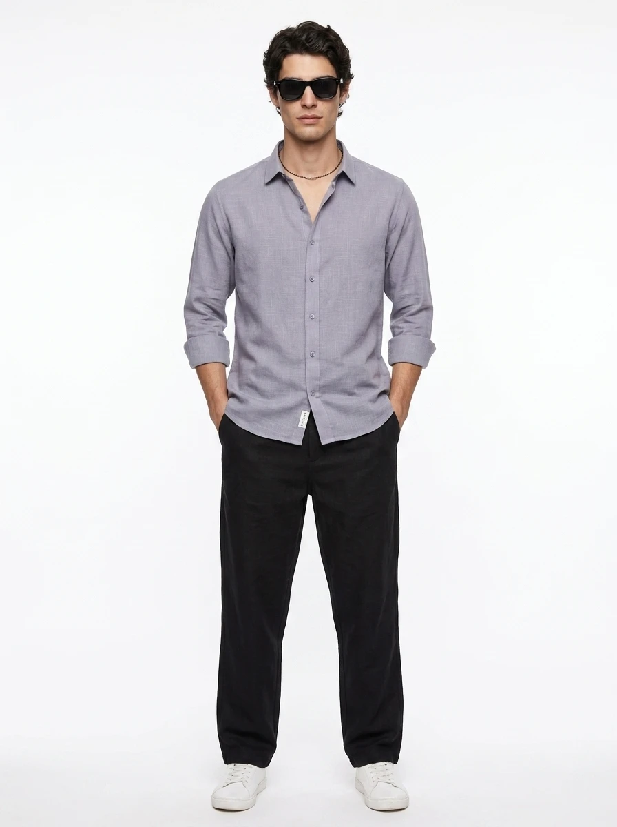 Man wearing a light purple long sleeve button up shirt, black trousers, and sunglasses standing against a white background.