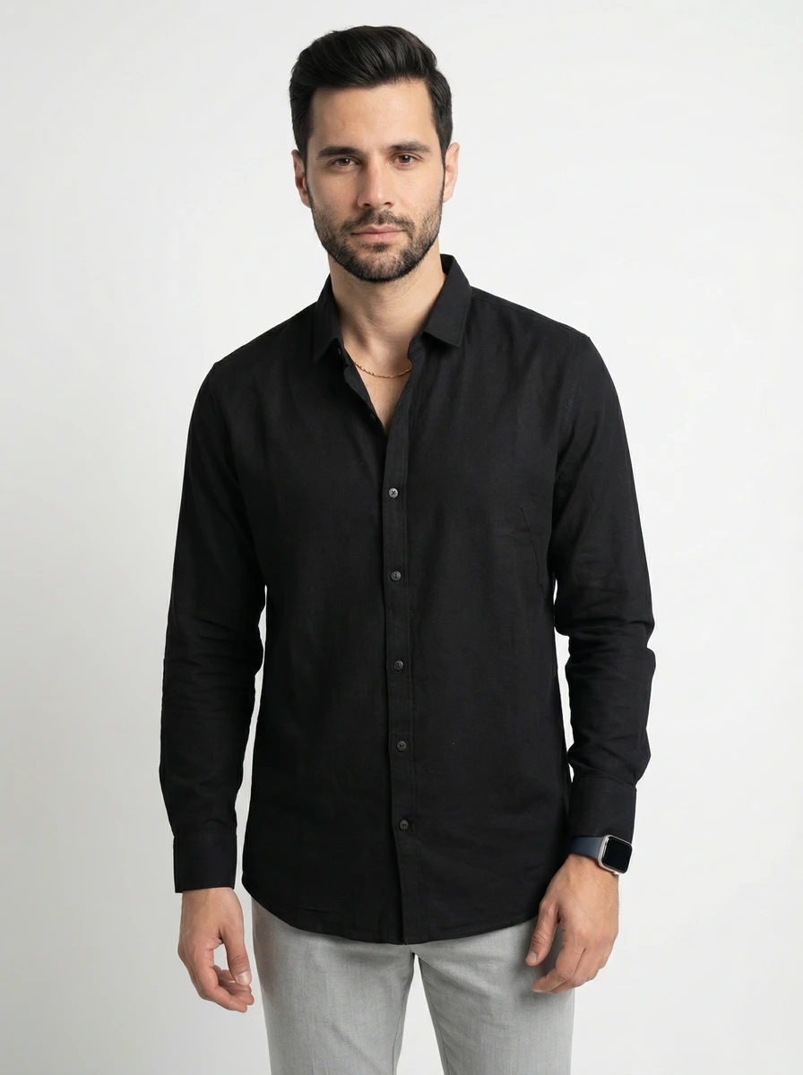 Man wearing a black long-sleeve button-down shirt and grey trousers against a plain white studio background.