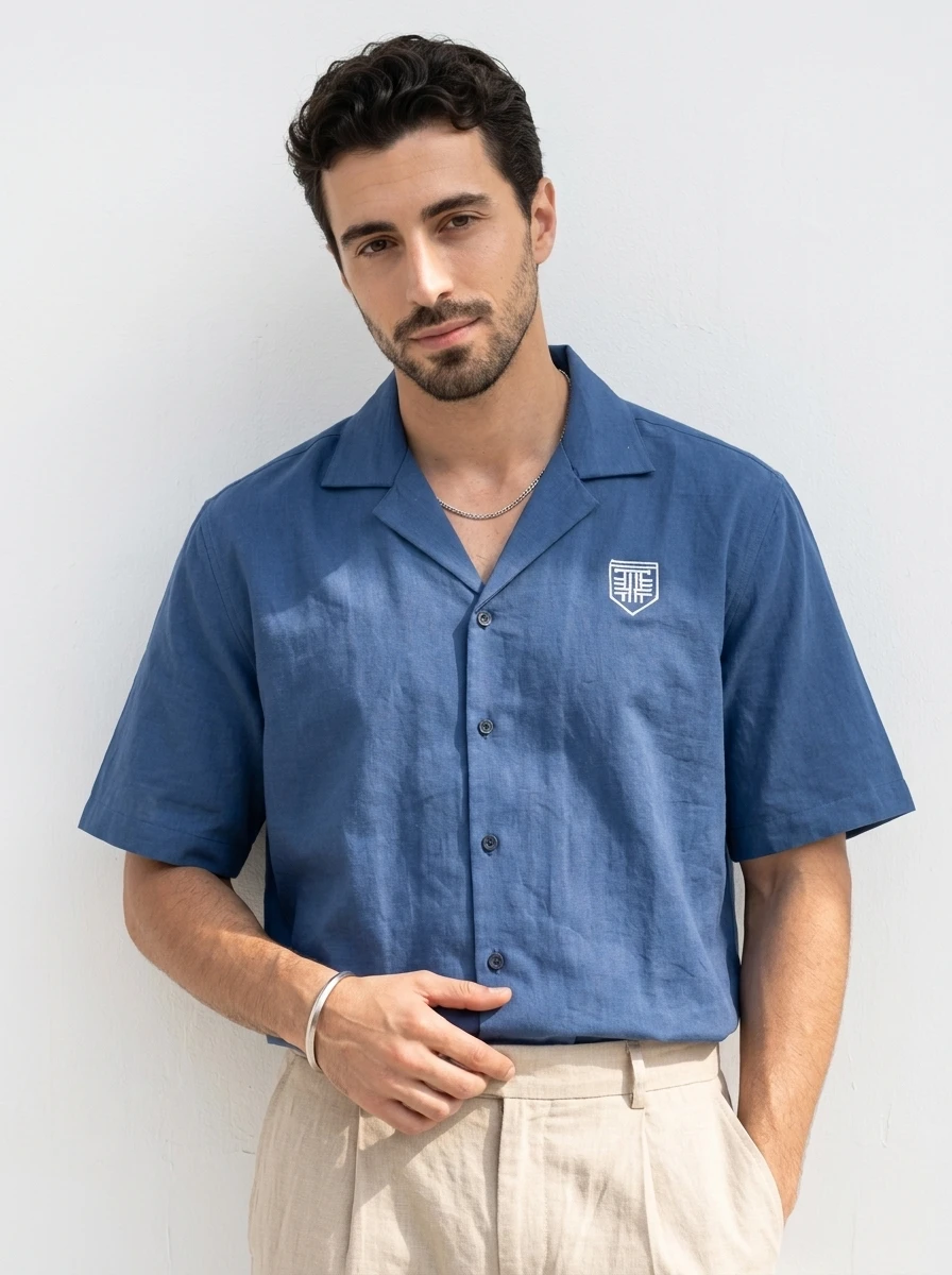 A man wearing a blue short-sleeve button-down shirt with a camp collar and white logo embroidery.