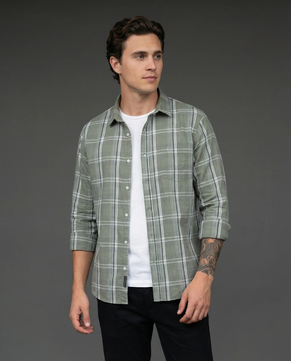 A man wearing an open green plaid button-down shirt over a white t-shirt against a grey background.
