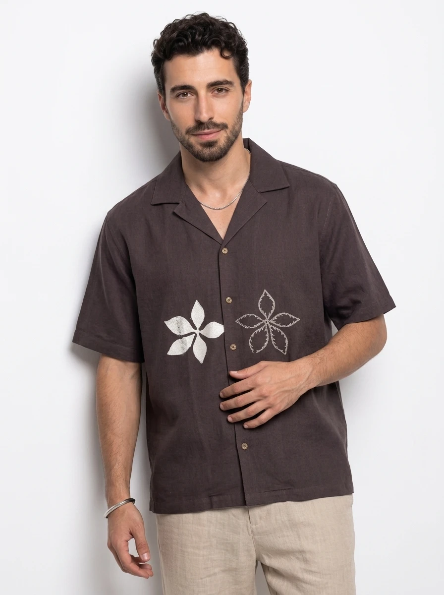 A male model wearing a dark brown short-sleeve button-down shirt with floral embroidery against a plain white background.