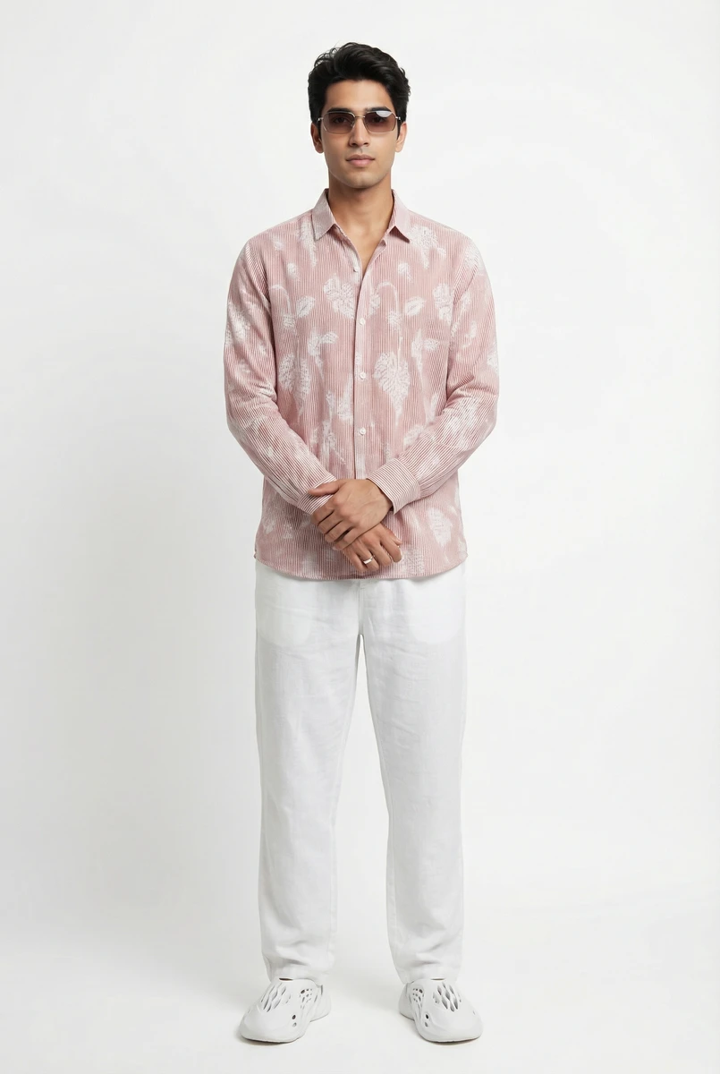 A man wearing a pink patterned long-sleeve shirt and white trousers against a plain white studio background.