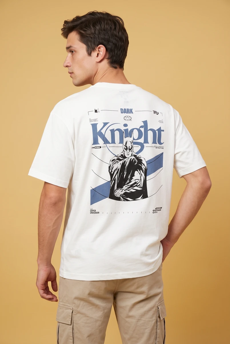 Male model wearing a white crew neck t-shirt with a blue and black Batman graphic print on the back against a tan background.