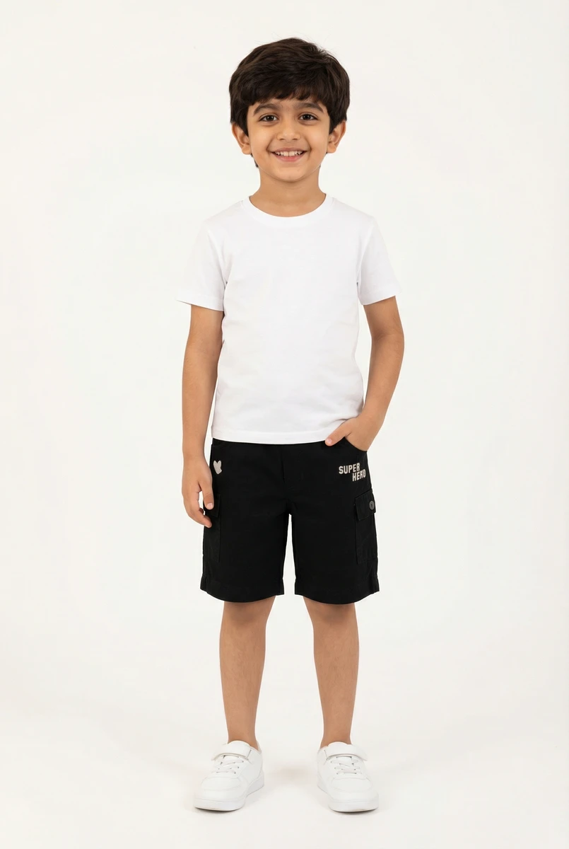 Young boy smiling in a plain white t-shirt, black cargo shorts, and white sneakers against a light background.
