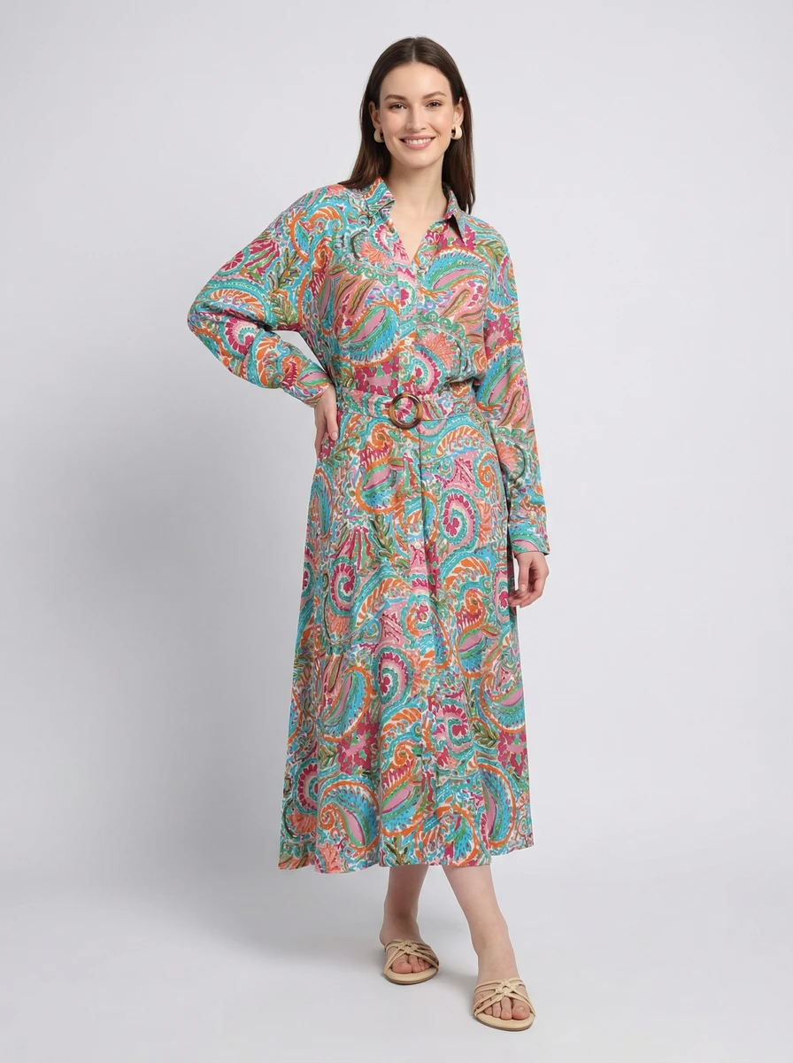 A woman posing in a long-sleeved midi shirt dress featuring a colorful paisley print and matching belt.
