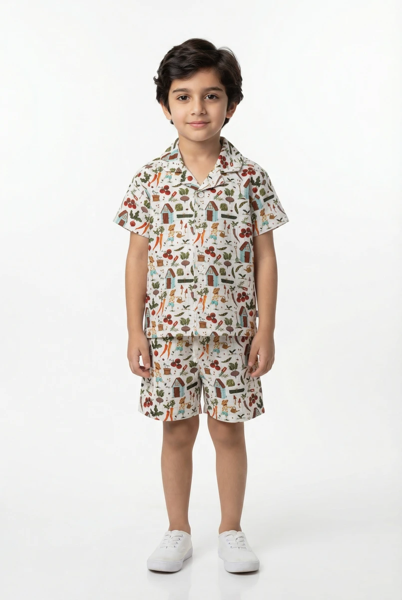 Young boy wearing a matching short-sleeve button-down shirt and shorts set with a colorful garden print against a white studio background.
