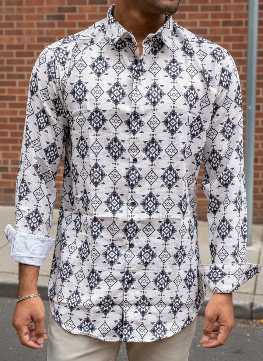 Man wearing a white long-sleeve shirt with a black geometric print outdoors against a brick wall.