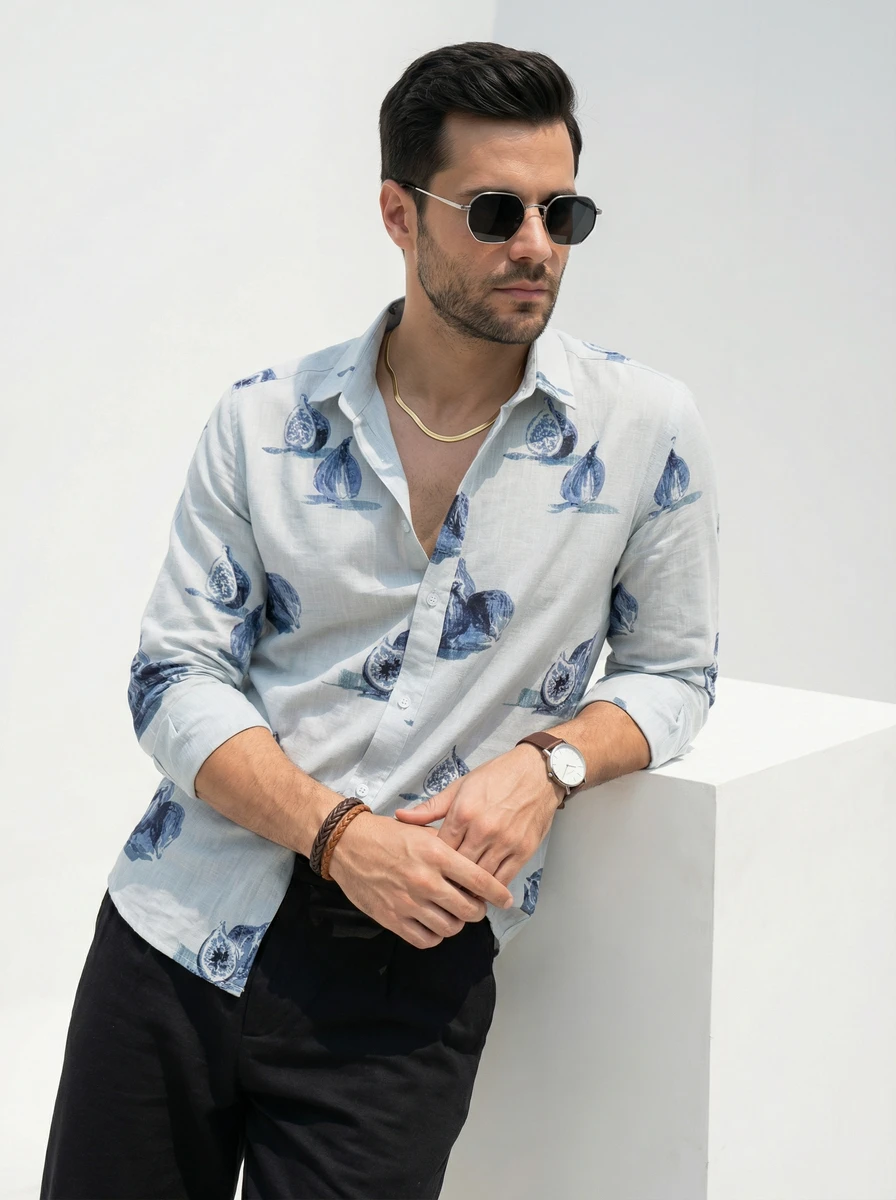 Man wearing a light blue button-down shirt with blue fig prints and black trousers, leaning against a white cube.