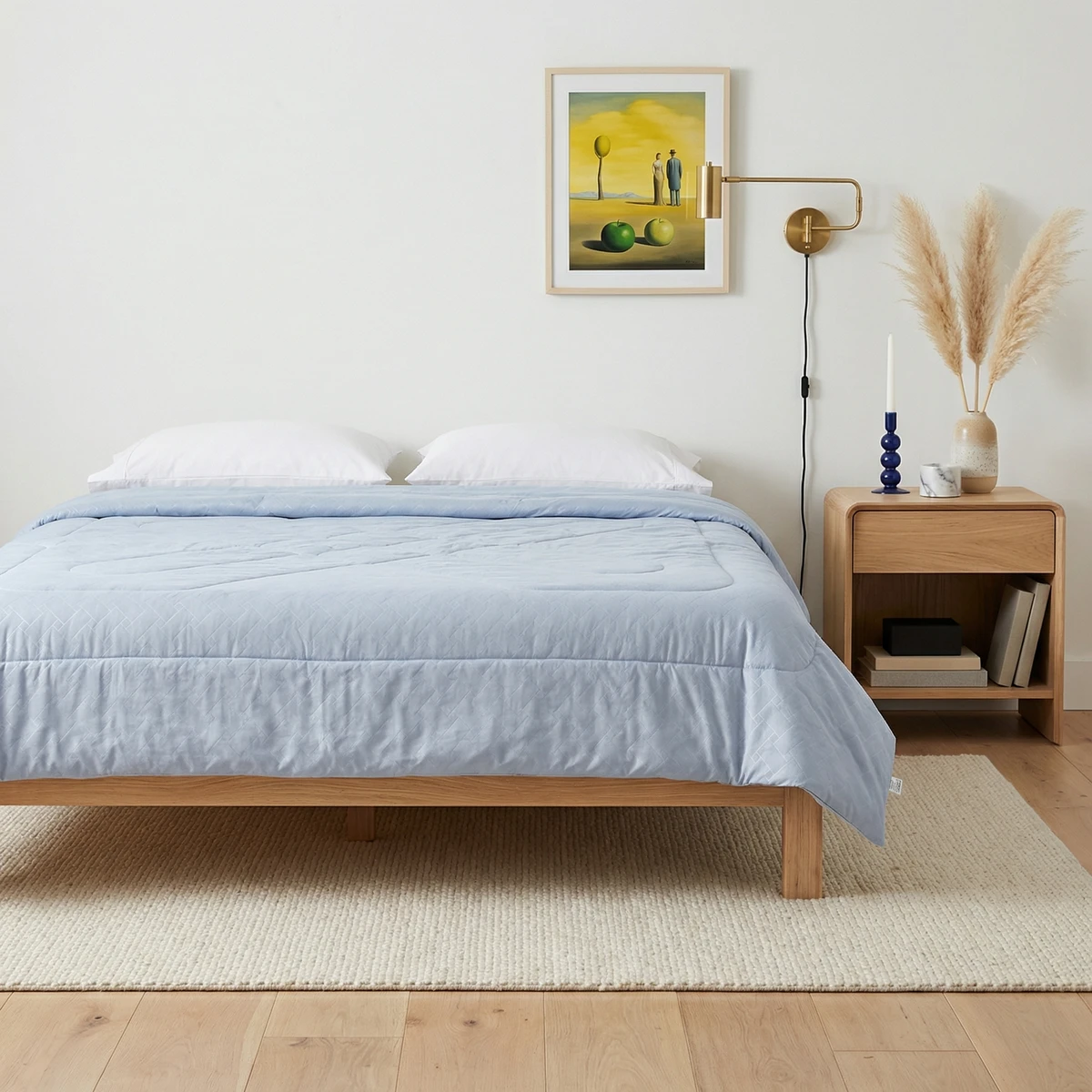 Light blue comforter on a wooden platform bed with white pillows, bedside table, and framed art.