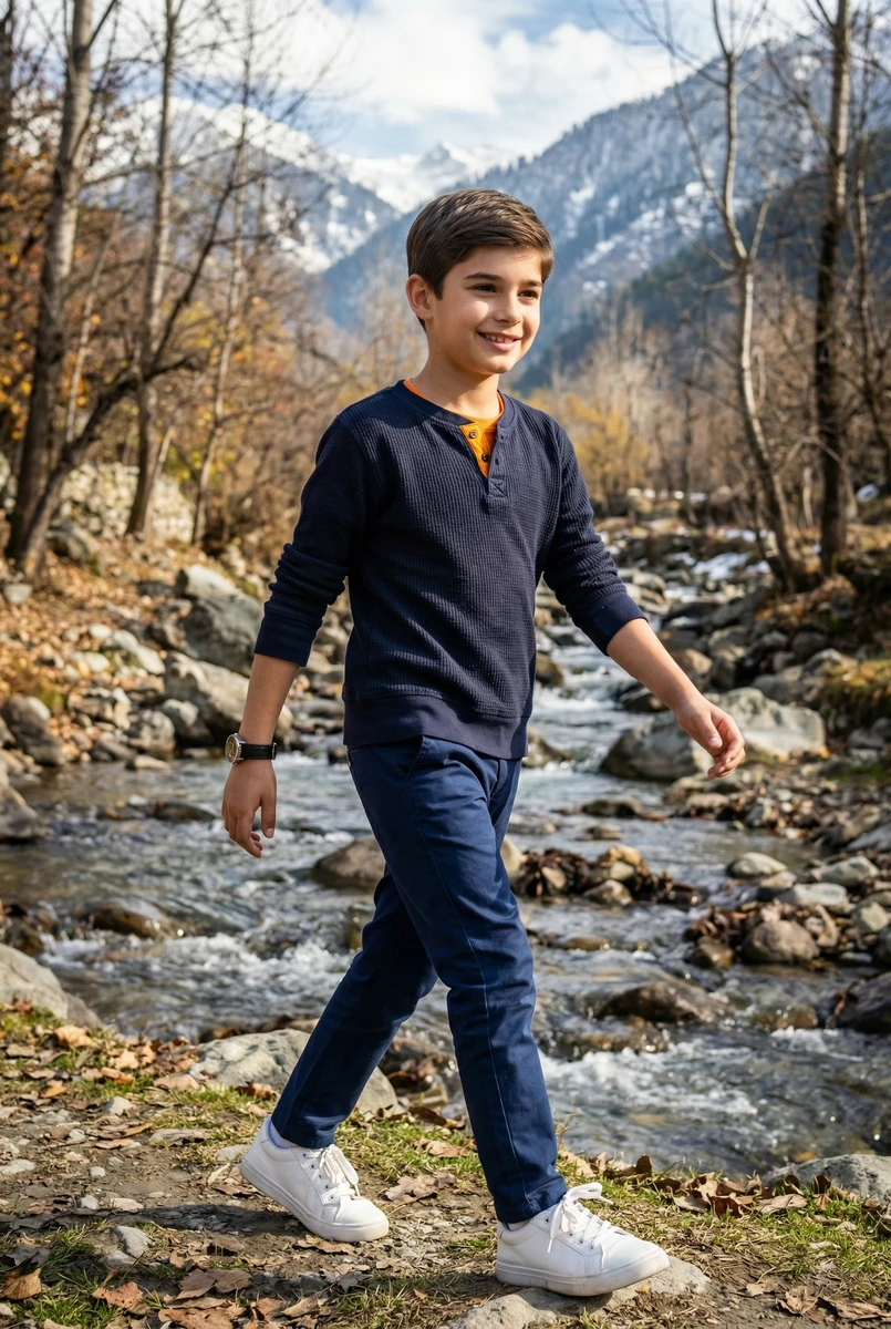 Young boy walking by a rocky stream wearing a navy waffle knit henley and blue pants.