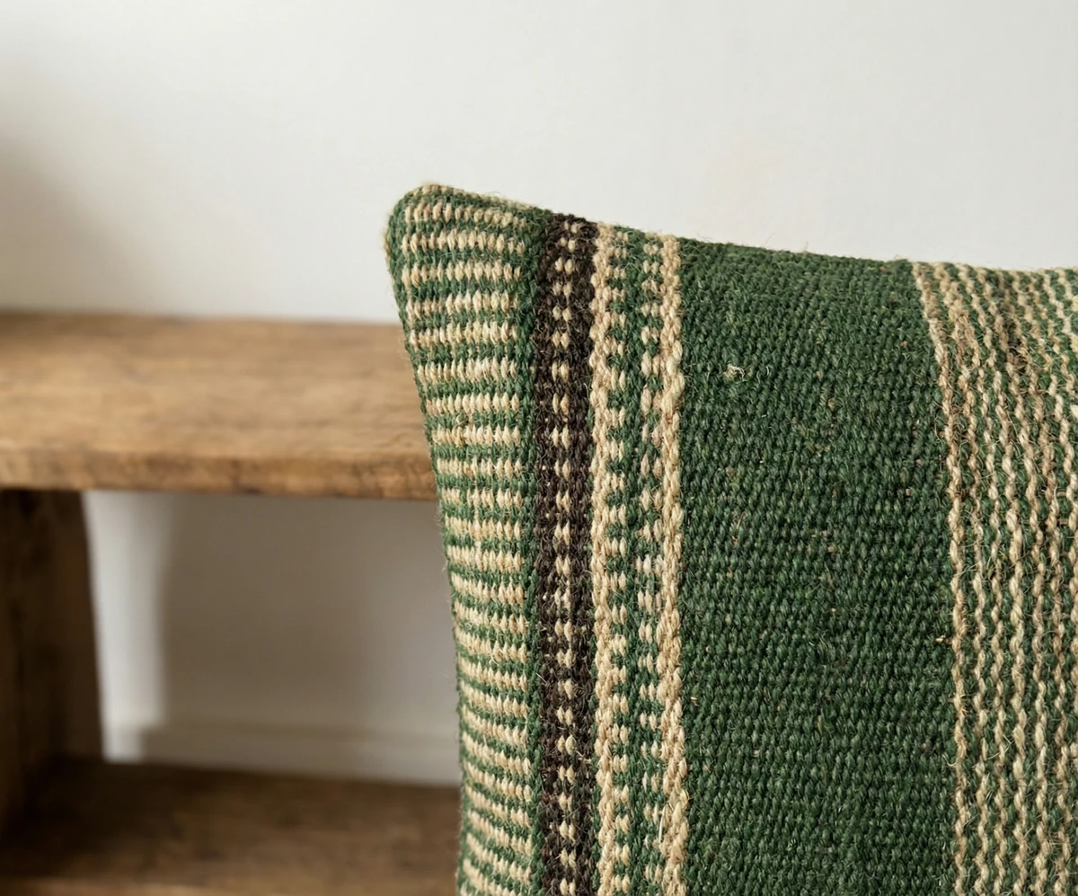 Close-up of a woven green and natural jute striped cushion against a wooden background.