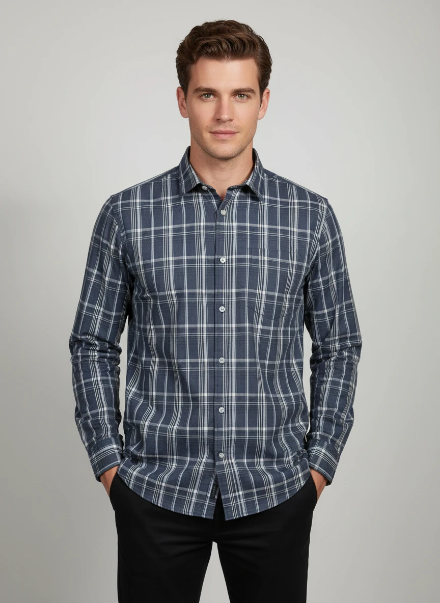 A man wearing a blue and white plaid long sleeve shirt and black trousers against a plain grey background.