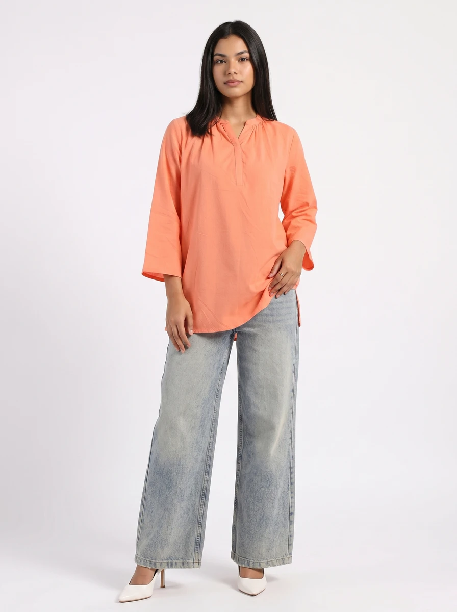 Model wearing a peach tunic top with three-quarter sleeves and light wash denim jeans.