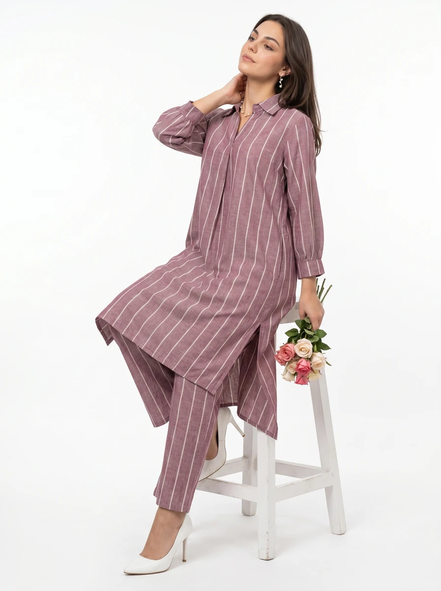 Woman wearing a mauve striped tunic and matching trousers, sitting on a stool holding a bouquet of flowers.
