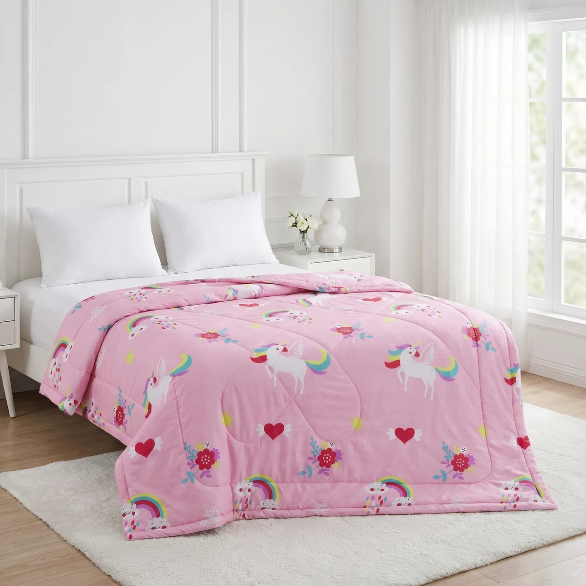 Pink comforter with unicorns, rainbows, and flowers spread over a white bed in a bright bedroom.