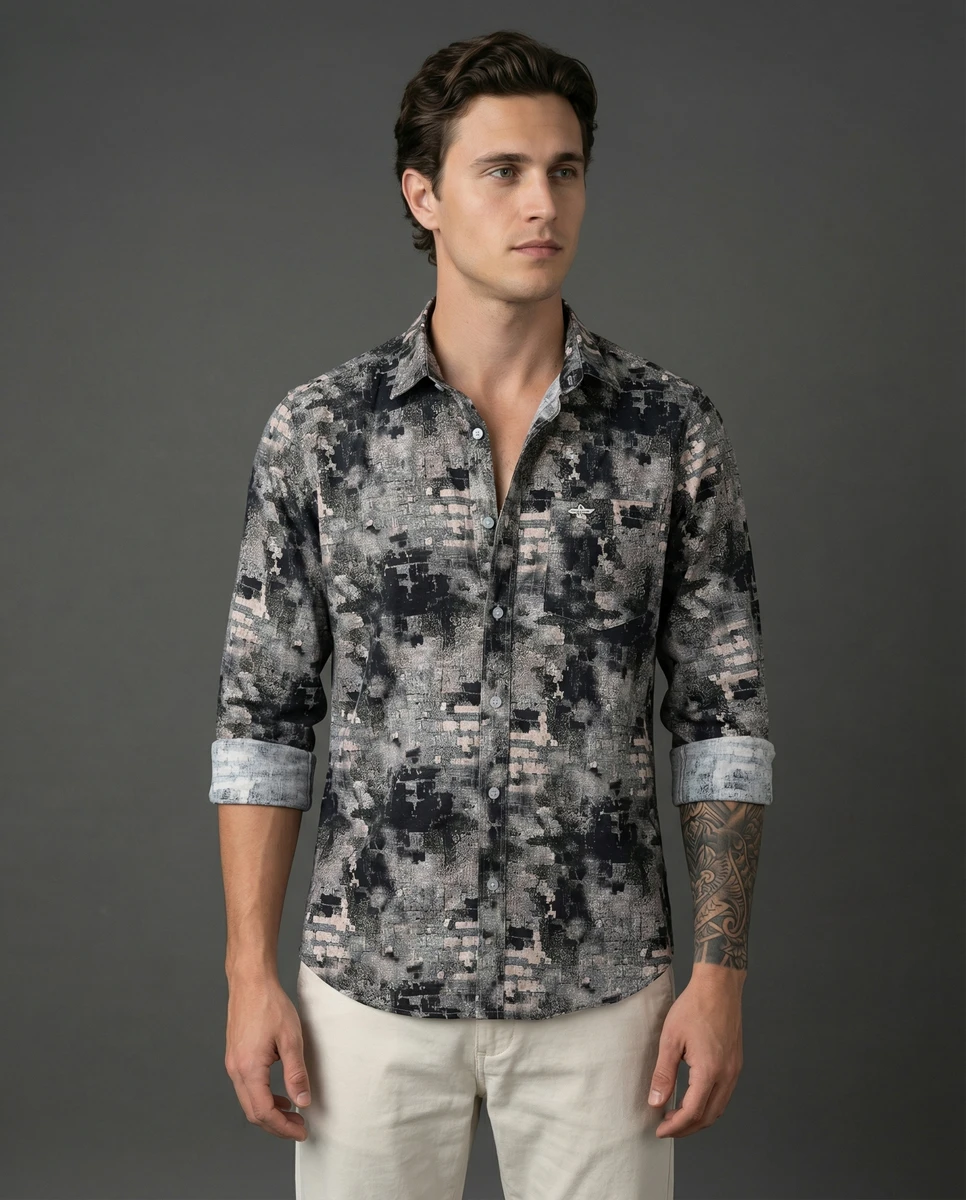 A male model wearing a grey patterned long-sleeve button-down shirt and off-white trousers against a dark grey studio background.