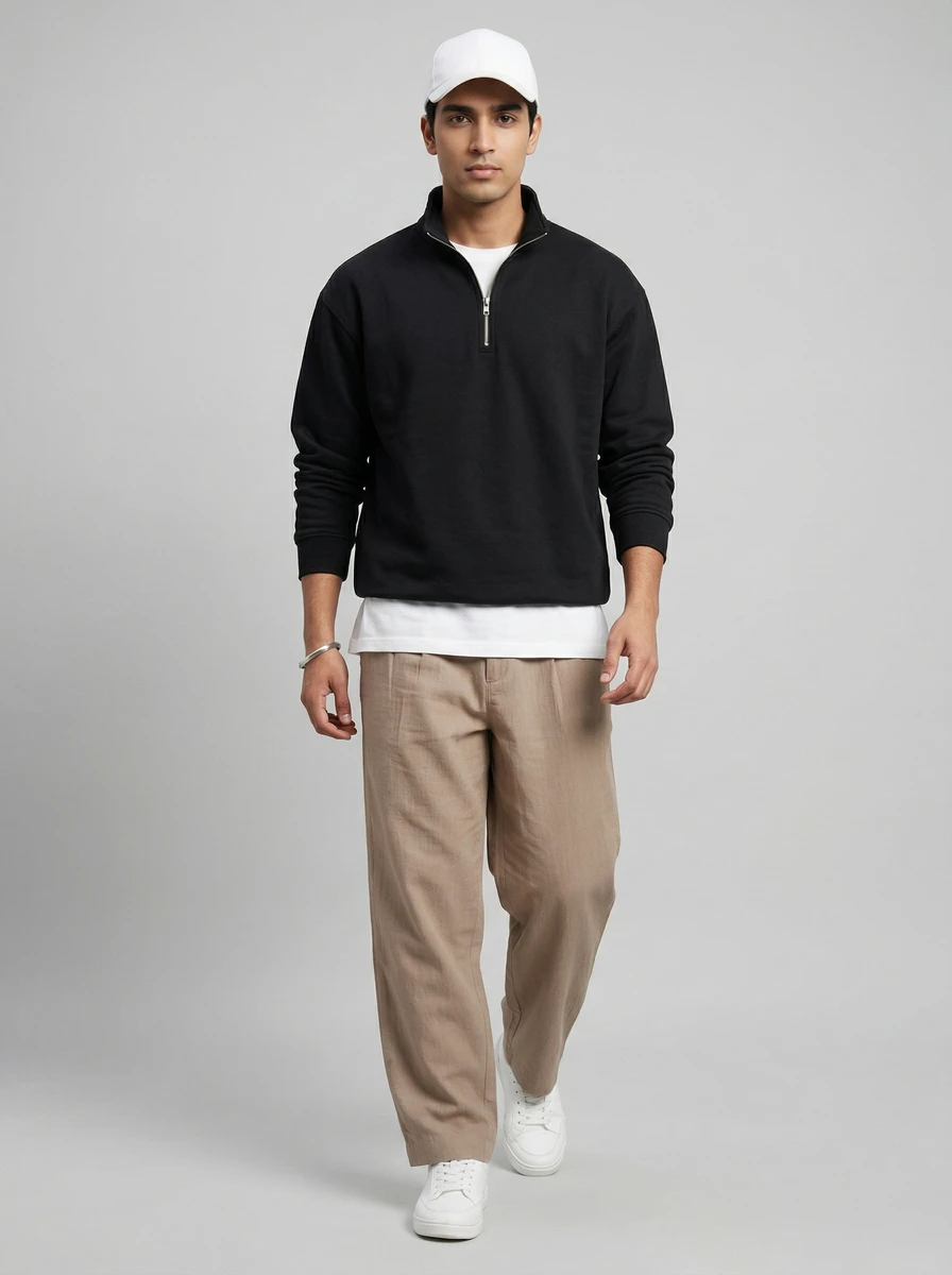 Man wearing a black quarter-zip sweatshirt over a white t-shirt, tan pleated trousers, and a white baseball cap.