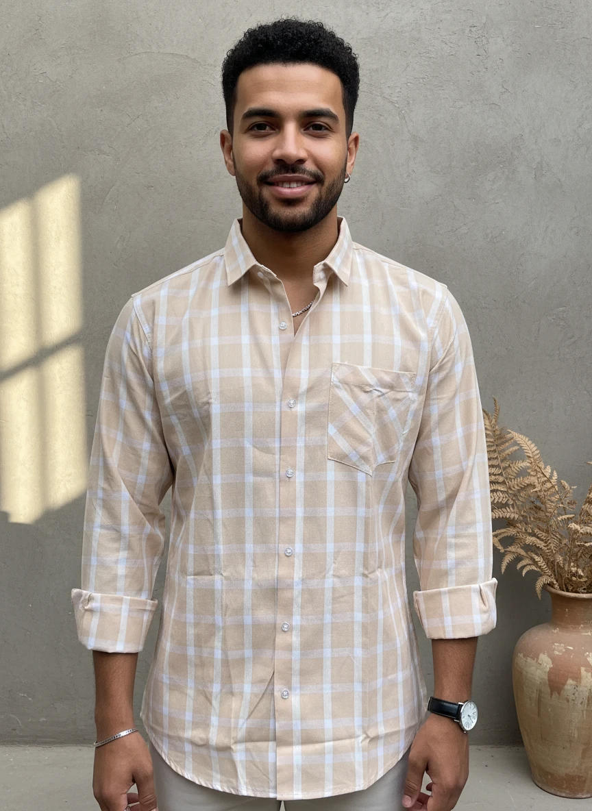 Man wearing a beige and white plaid long-sleeve button-down shirt with a chest pocket, posing against a textured gray wall.