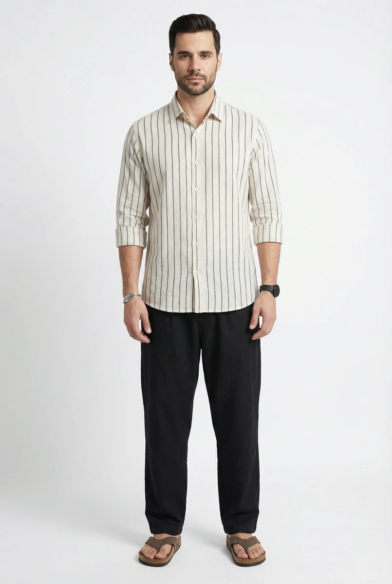 Man standing in white striped button-down shirt and black trousers against a white studio backdrop.