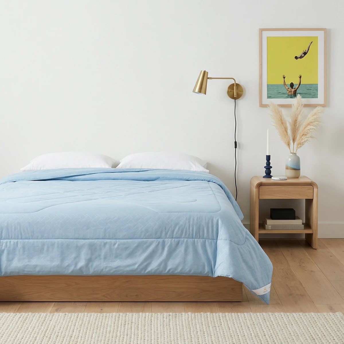 Light blue comforter on a wooden bed frame in a brightly lit bedroom with a nightstand and wall art.