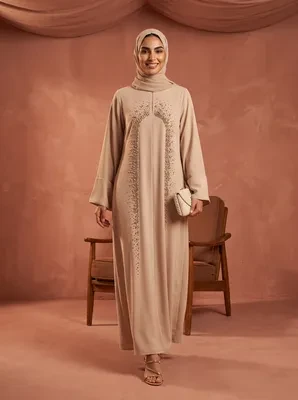 Model wearing a beige long sleeve abaya with beaded embroidery, matching hijab, and holding a small handbag.